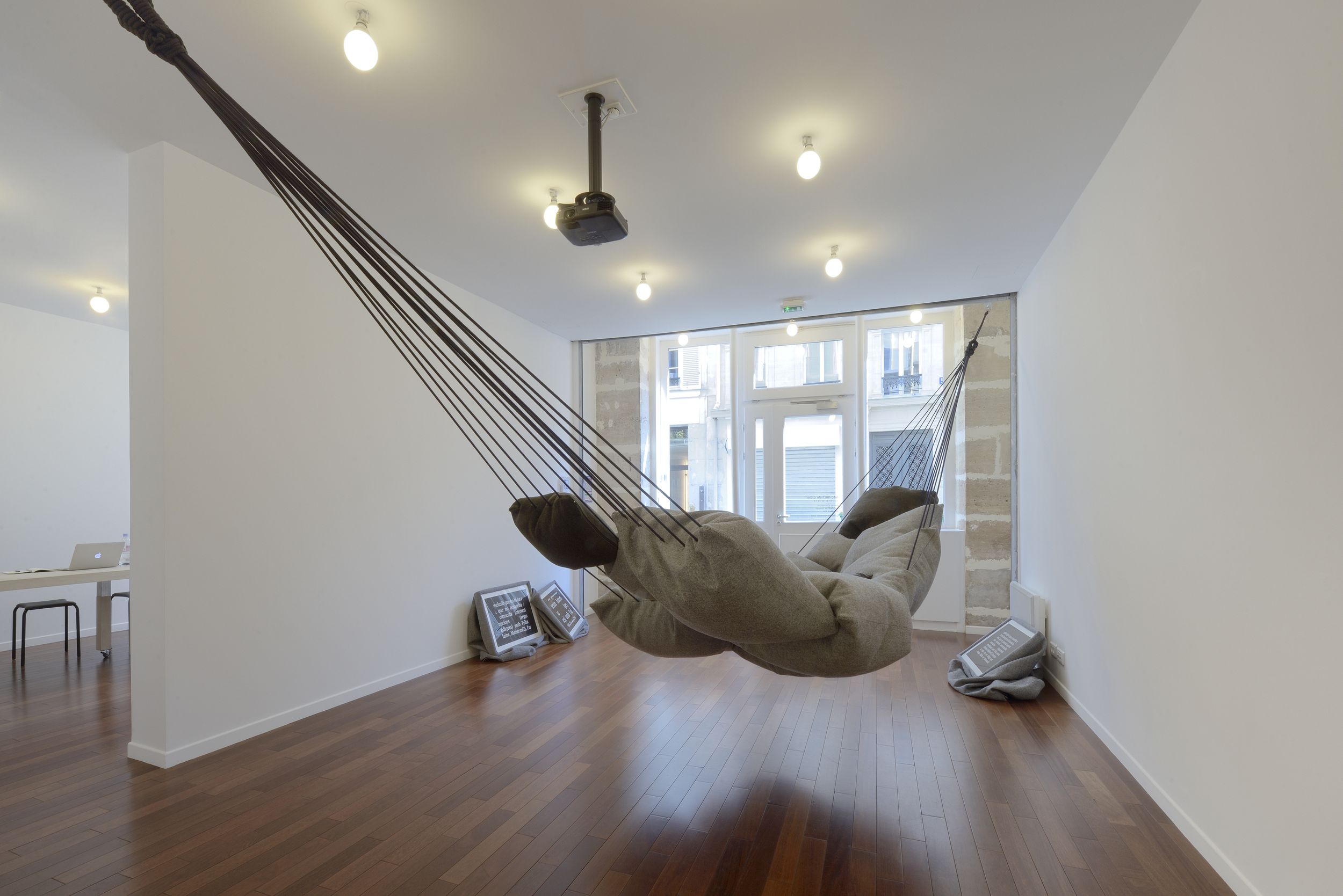 A suspended pillow hammock and text-covered pillows in the BLESS Contenttenders exhibition in Paris.