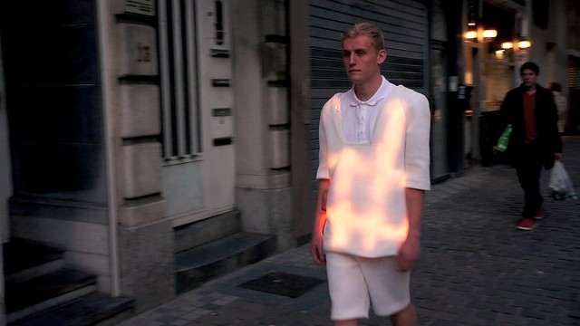 A performer wearing the illuminated Wearable Facade garment walks through a Brussels street.