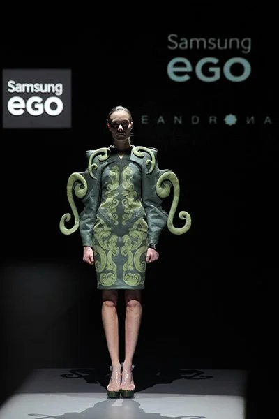 Model wearing a fitted green dress with large curled sculptural elements from 083
