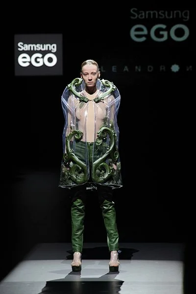 Model wearing a transparent cape with green sculptural details from 083