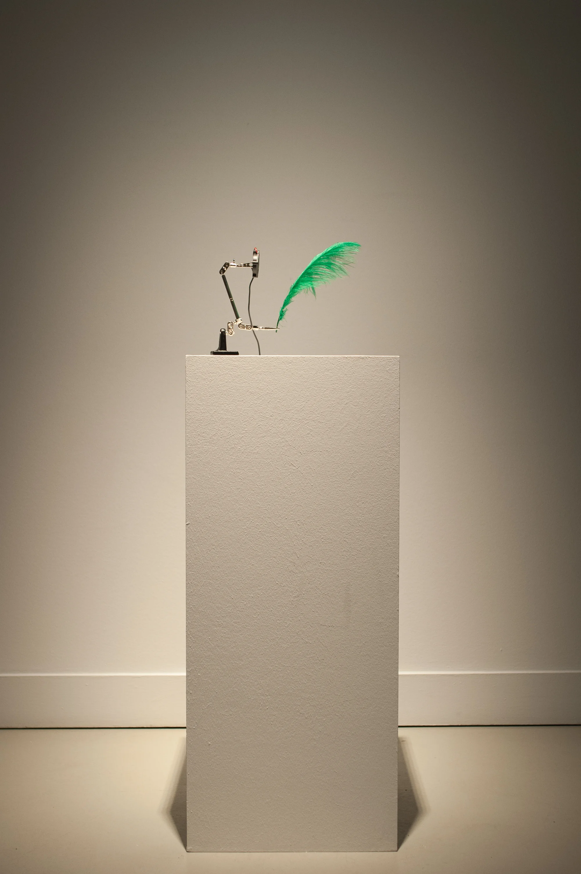 Vertical exhibition view of the green feather sculpture on a white plinth