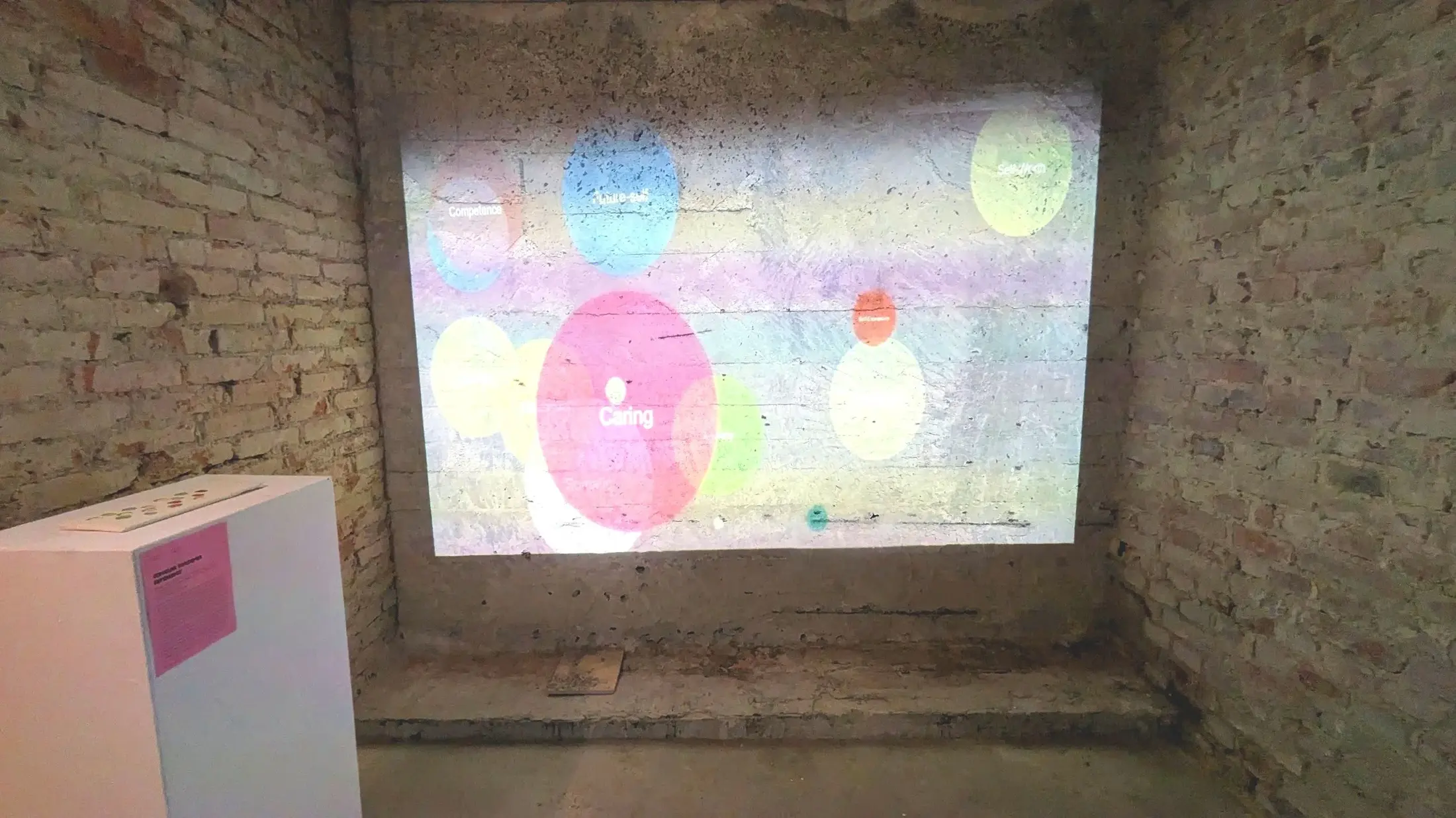 Enquête d’âme installed in a brick-walled exhibition space with a tactile console facing a projection of translucent coloured circles