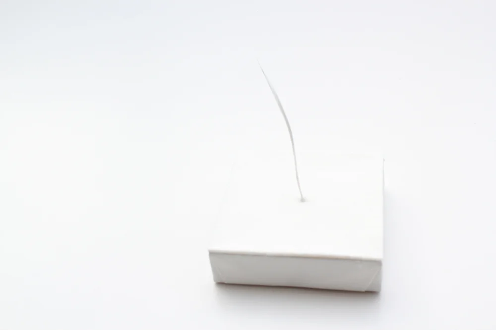 A single white feather resting almost invisibly on the white Feather Tales block