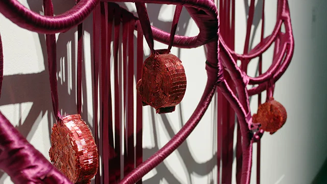 Close view of two red beaded hearts suspended within the magenta structure