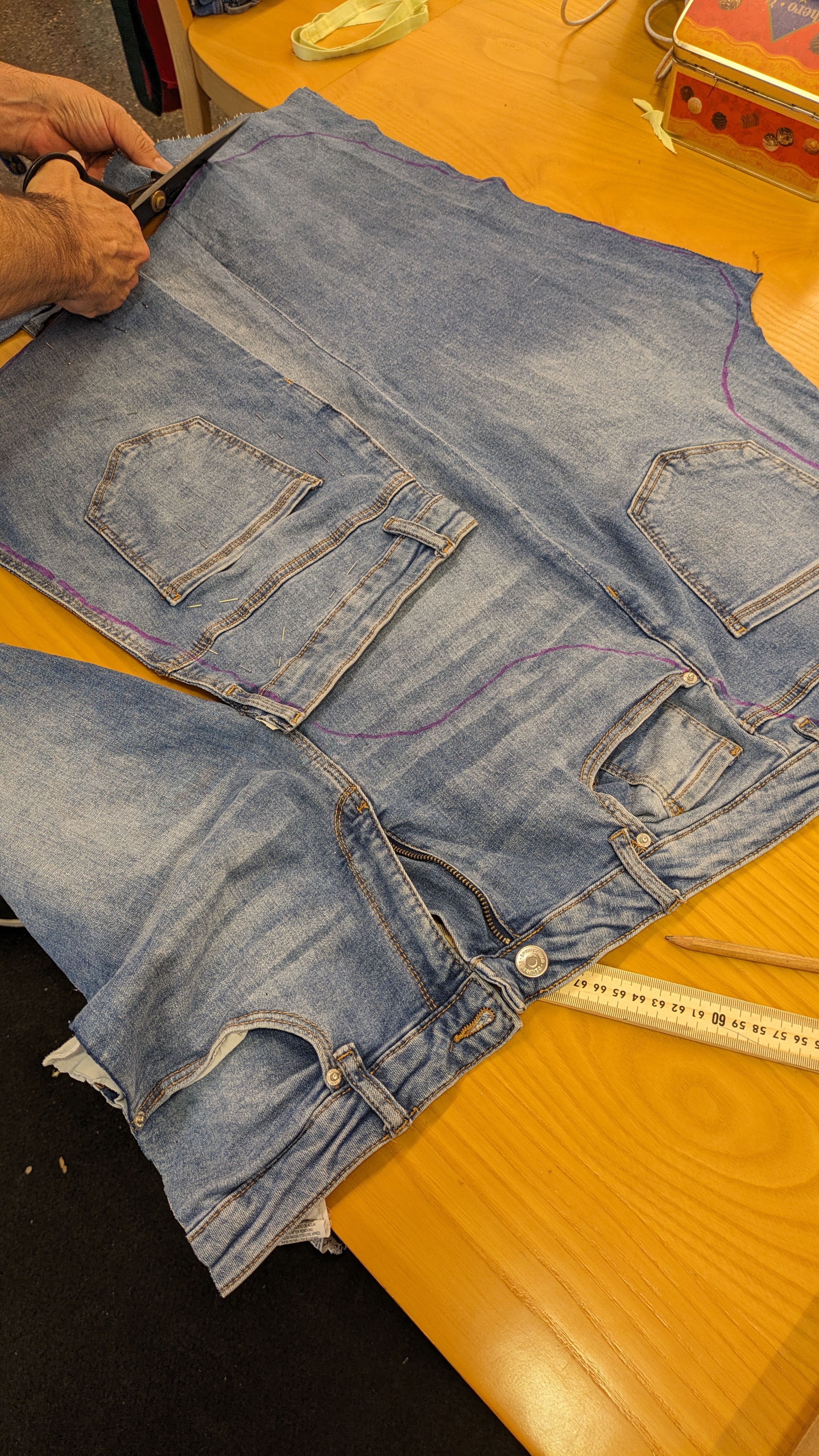 Hands cutting reused denim trousers on a worktable while developing the Upcycling 2.0 costume