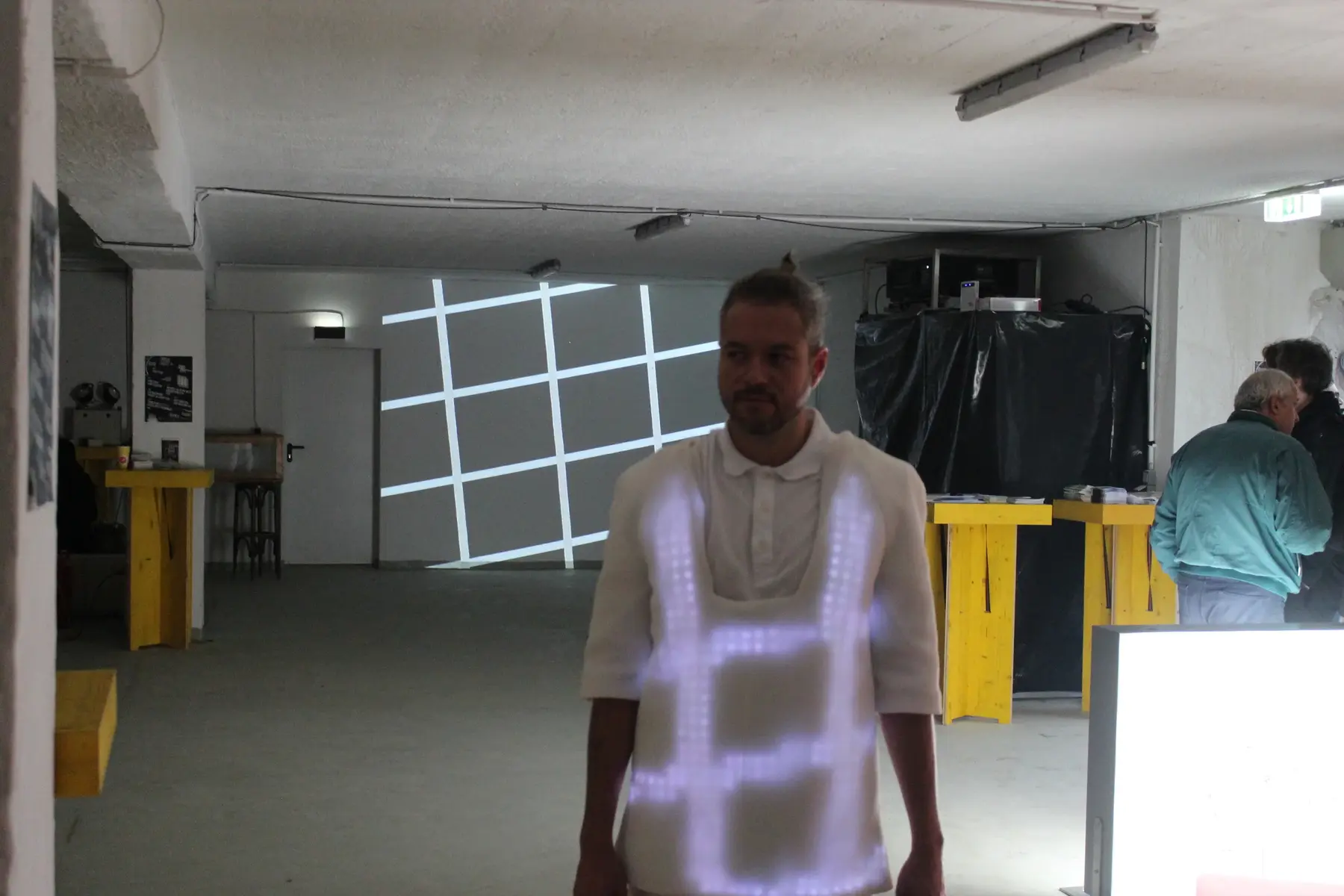 A performer in the illuminated garment standing before a large projected grid pattern