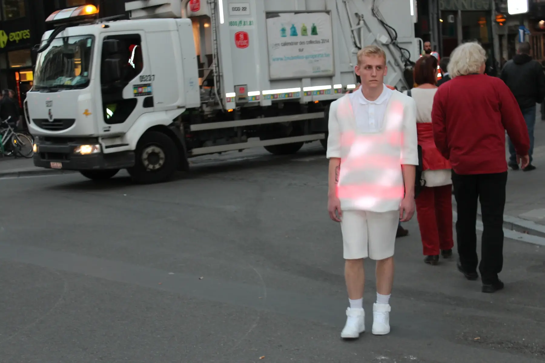A performer wearing the glowing white garment while standing on a busy Brussels street